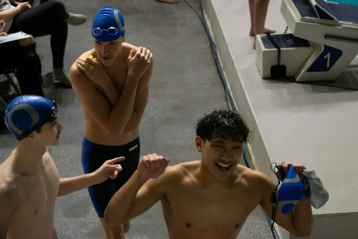 Club swimmers on poolside beside the starting blocks at an indoor pool after a session